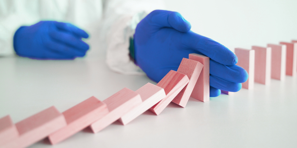 A hand wearing a blue glove stopping dominoes from falling any further