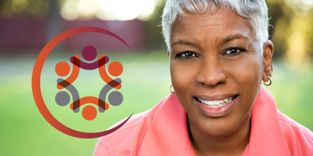 An adult African American female with grey hair wearing a pink top and smiling