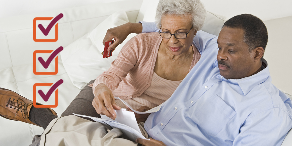 An adult African American male putting his arm around an adult African American female while holding credit cards and looking at documents