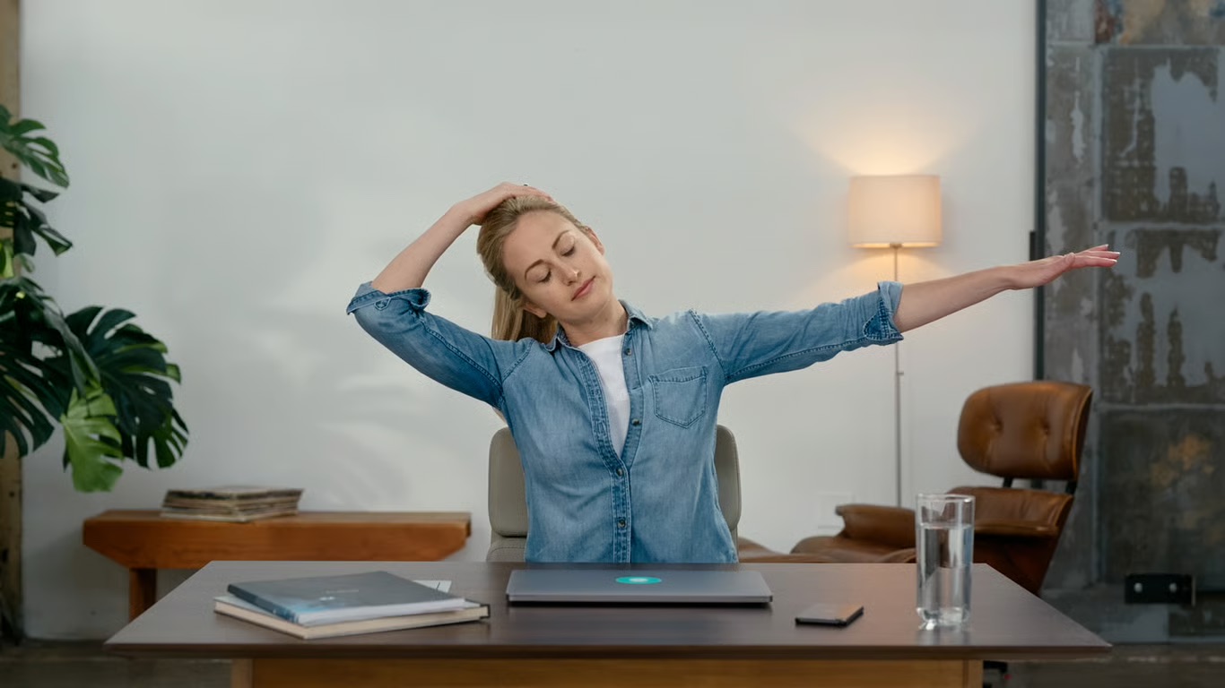 A woman sitting at a desk and stretching her neck